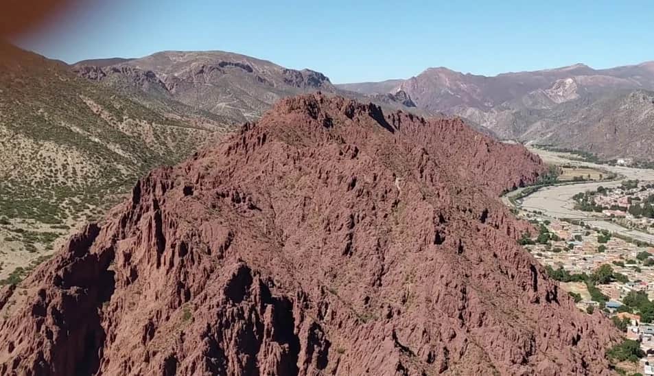 Paisaje de cordillera árida con un pueblo en el valle bajo un cielo despejado, como metáfora de reunión entre regiones.