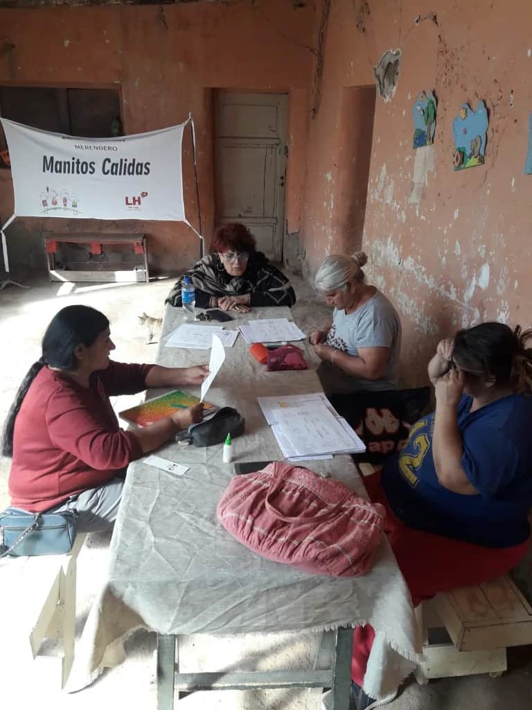 Merendero Manitos Cálidas: mujeres trabajando en equipo en una mesa con documentación y materiales en el espacio comunitario.